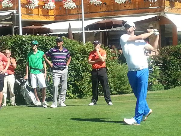 Michael Phelps drives off the first as Richie Ramsay (orange shirt) looks on. (Photo - www.golfbytourmiss.com)