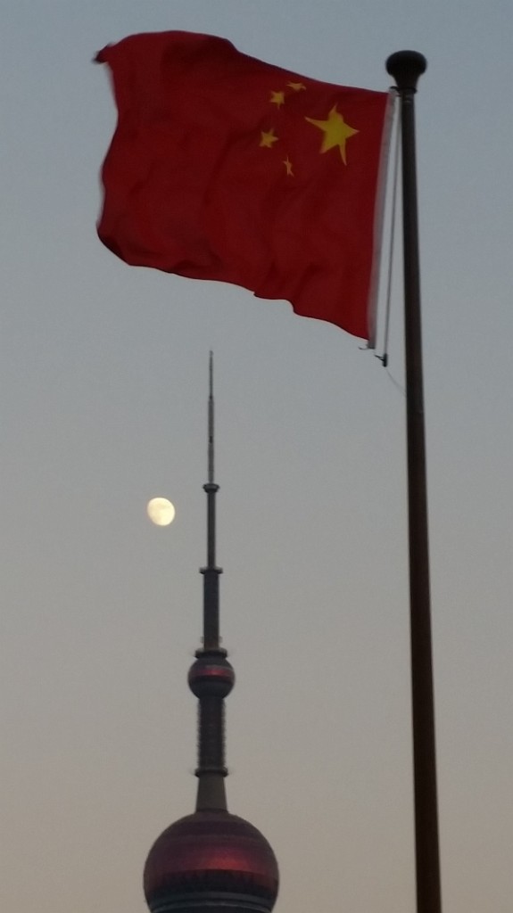 The Chinese flag flutters in the foreground as a full moon heads towards the Oriental Pearl Tower.